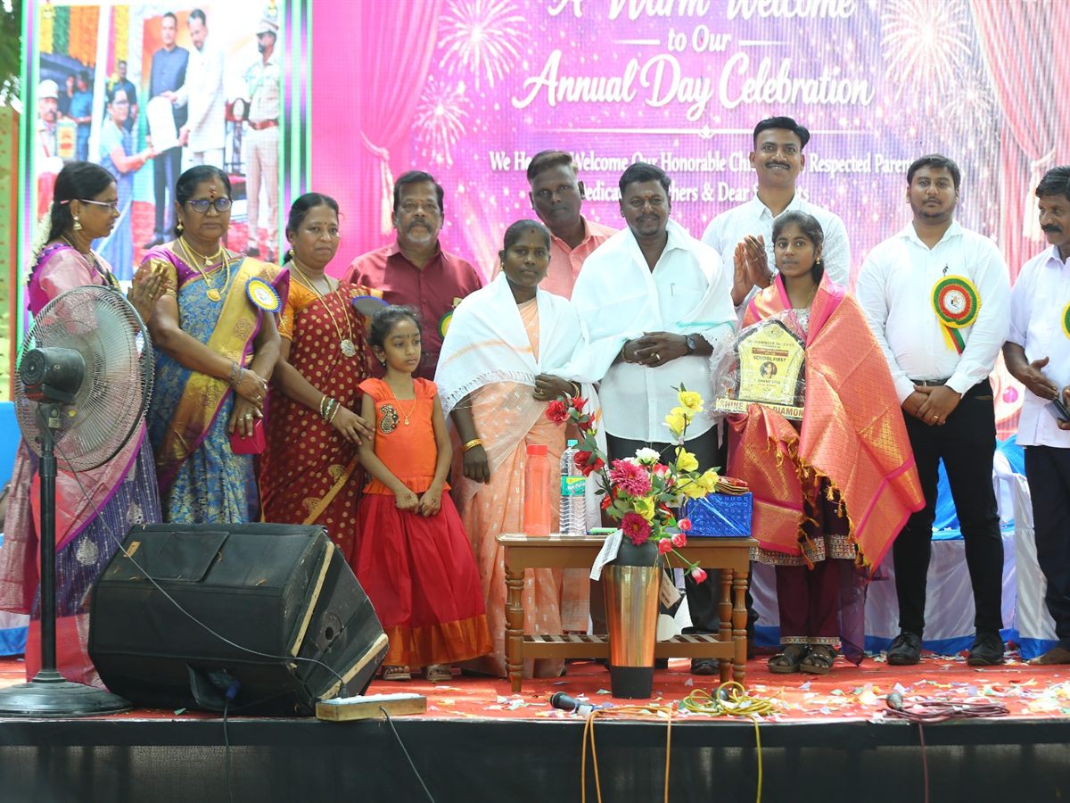 The school-first student holding her trophy on the Annual Day stage with her family and teachers