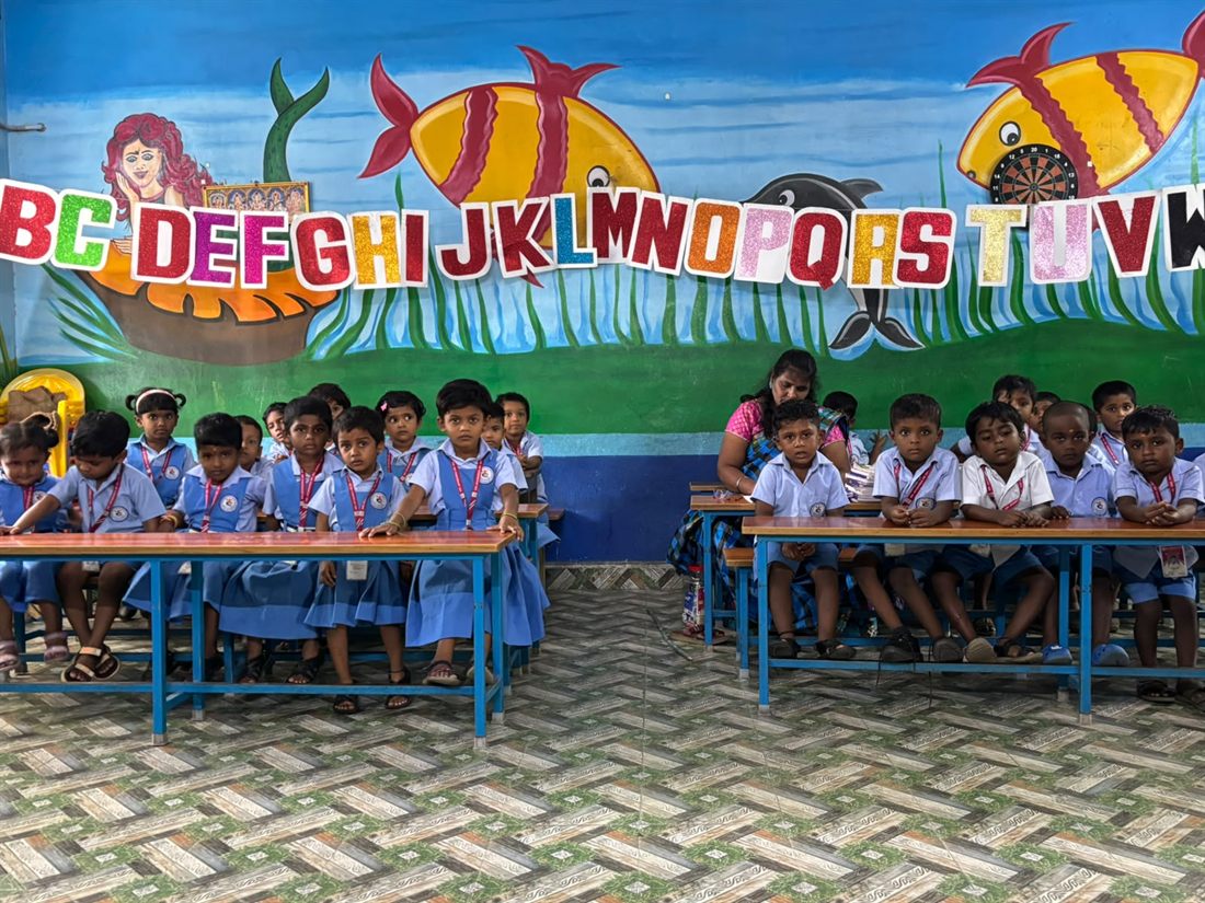 The kindergarten class at their desks, the alphabet painted along the wall