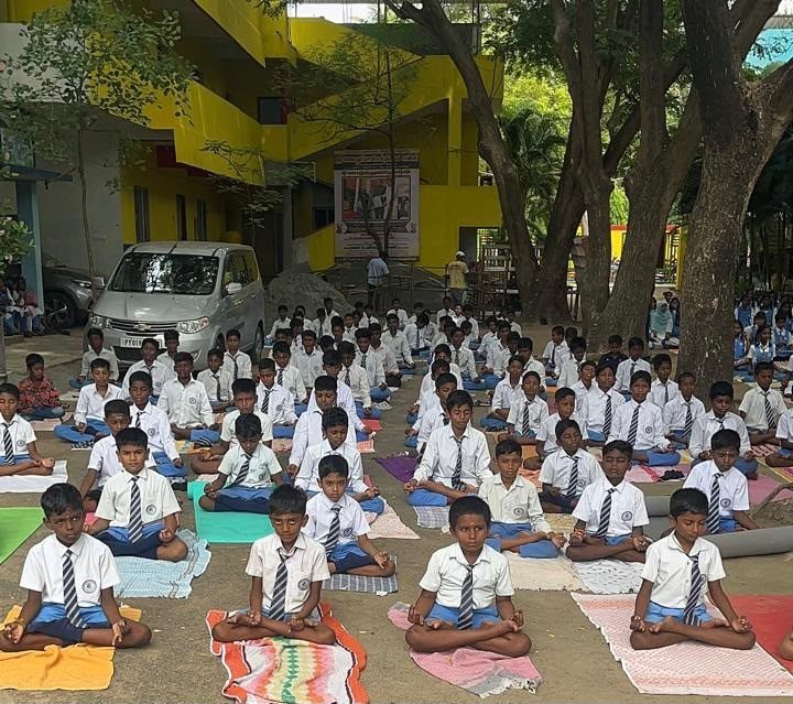 Students seated on mats in the shade for Yoga Day
